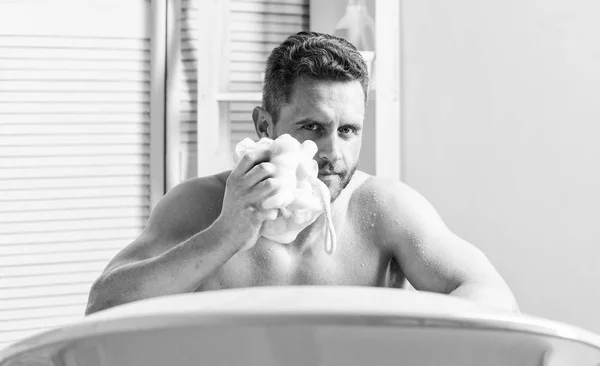 Sich mit einem heißen oder warmen Bad zu verwöhnen, kann sich wie Luxus anfühlen. Mann schöner muskulöser Kerl, der sich in der Badewanne entspannt. Verwöhn- und Schönheitsroutine. Hautpflegekonzept. Bad mit Seifenlauge — Stockfoto