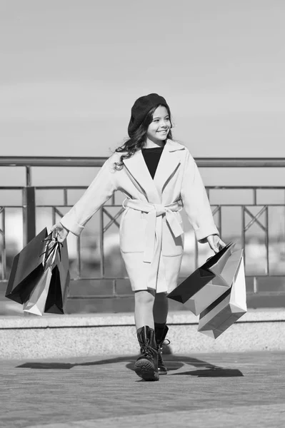 Día de compras satisfactorio. Niño elegante bodega manojo bolsas de compras. Chica lindo abrigo de señora y boina llevar bolsas de compras. Concepto de compras de primavera. Comprar ropa y accesorios para la temporada de primavera — Foto de Stock