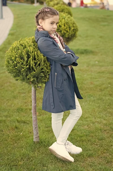 Must have concept. Fashionable coat. Girl cute face braided hair posing coat in spring park. Clothing for spring walks. Little fashion model. Clothes and accessory. Kid wear trench coat. Spring coat