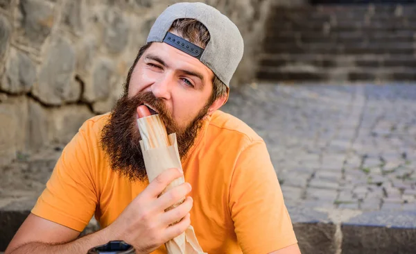 Despreocupado hipster comer junk food while sit on stairs. Um lanche de homem faminto. Comida de plástico. Um tipo a comer cachorros quentes. Homem barbudo mordida saborosa salsicha e beber copo de papel. Comida de rua tão boa. Estilo de vida urbano nutrição — Fotografia de Stock