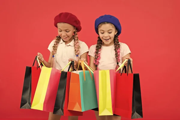 Kinderen tevreden met winkelen rode achtergrond. Geobsedeerd door winkels en kledingwinkels. Winkelverslaafd concept. Winkelen wordt leuk met beste vrienden. Kinderen schattig schoolmeisjes houden bos boodschappentassen — Stockfoto