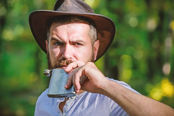 Wild West is his heart. camping and hiking. mature male with brutal look drink alcohol from flask. Bearded man in cowboy hat in park outdoor. man hipster relax in autumn forest. Spring sunny weather — Stock Photo, Image
