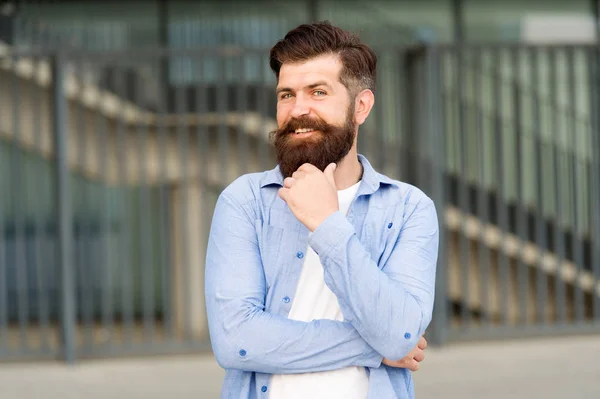 Having extensive facial hair growth. Happy hipster with stylish beard and mustache hair on urban background. Bearded man smiling with unshaven face hair. Brutal guy with shaped beard and styled hair