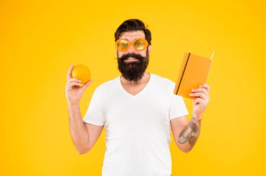 Vitamin kaynağı. Tam bir portakal. Adam uzun sakal turuncu renk seviyor. Parlak ve canlı. Adam sakallı neşeli gülümseyen hipster turuncu renk güneş gözlüğü giymek ise turuncu meyve ve kitap not defteri tutun