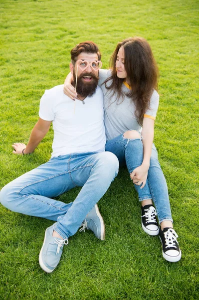 Innamorarsi. Uomo barbuto guardando con amore attraverso occhiali puntello a forma di cuore. Coppia sensuale innamorata di rilassarsi su erba verde. Donna sexy e hipster avere una storia d'amore — Foto Stock