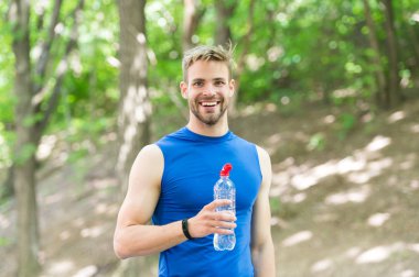 Sağlıklı bir yaşam tarzı. Tazeleyici içecek. Sporcu adam elinde şişe suyu tutuyor. Sporcu parktaki eğitimden sonra su içer. Vitamin ve mineraller. Erkek sporcu kıyafetleri su dengesini önemser.
