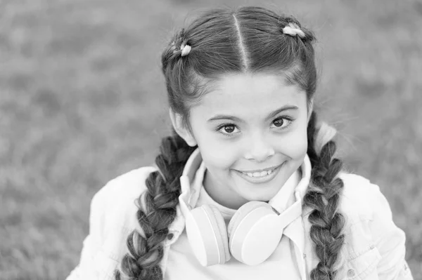 Enfant heureux émotionnel sain se relaxant à l'extérieur. Ce qui rend l'enfant heureux. Coiffure de fille tresses et écouteurs modernes profiter de se détendre. Secrets pour élever un enfant heureux. Fille mignon enfant vert fond d'herbe — Photo