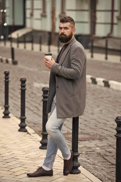 Relaxing coffee break. Hipster hold paper coffee cup and enjoy urban environment. Drink it on the go. Man bearded hipster prefer coffee take away. Businessman drink coffee outdoors. Reloading energy