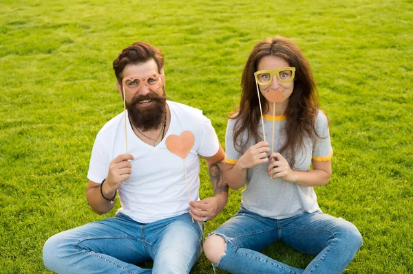 His heart belongs to her. Bearded man giving her a loving heart. Couple in love having photobooth party on green grass. Sexy woman and hipster with red heart holding props. One heart two souls
