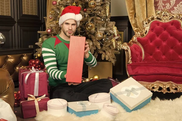 A very happy Christmas to you. Happy man with Christmas gift boxes. Guy is celebrating Christmas at home. Man in santa hat hold xmas presents. Delivery Christmas gifts