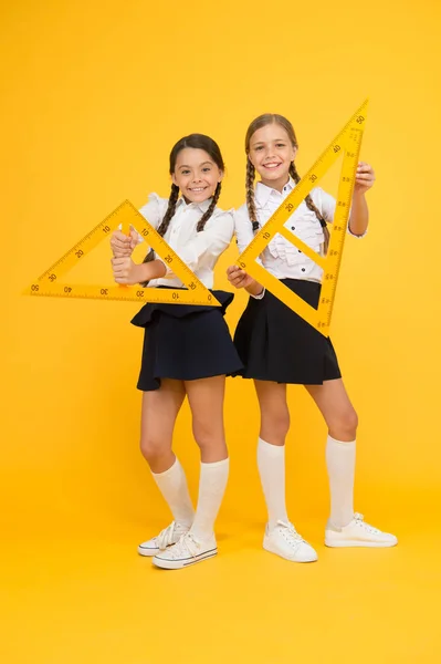 Formas geométricas. las pupilas usan gon ruler. disciplinas del tallo. de vuelta a la escuela. Matemáticas y geometría. Niños con uniforme en la pared amarilla. amistad y hermandad. niñas pequeñas feliz estudio de matemáticas —  Fotos de Stock