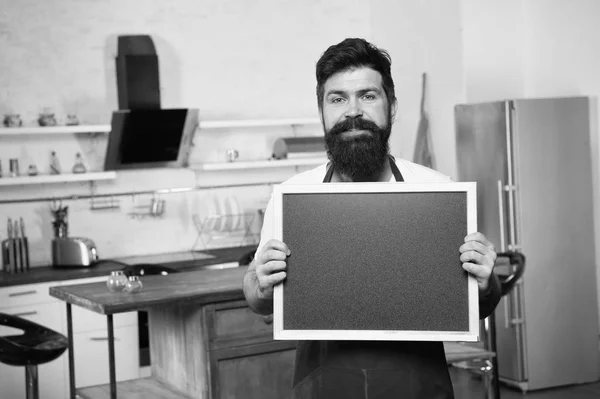 Chef at work. I need you at the kitchen. Hipster in kitchen. Mature male. Bearded man cook. Bearded man in red apron. Man chef with board, copy space. Restaurant or cafe menu. Advertisement