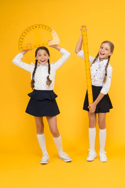 式。学校に戻る数学と幾何学黄色い壁に制服を着た子供たち。友情と姉妹関係。幸せな小さな女の子は数学を勉強します。学生は分度器定規を使用します。ステム規律 — ストック写真