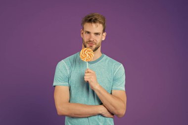 Çocukluk tadına. Adam yakışıklı maço büyük renkli tatlı lolipop yemek. Kıl adamla Lolipop sever. Yemek kavram hile. Şeker sağlık için zararlı. Adam tutun lolipop şeker menekşe arka plan