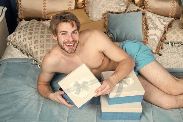 Opening his present. Handsome guy with box on birthday morning. Sexy man smiling with birthday gift in bed. Happy man holding birthday present wrapped in box. Happy birthday to you