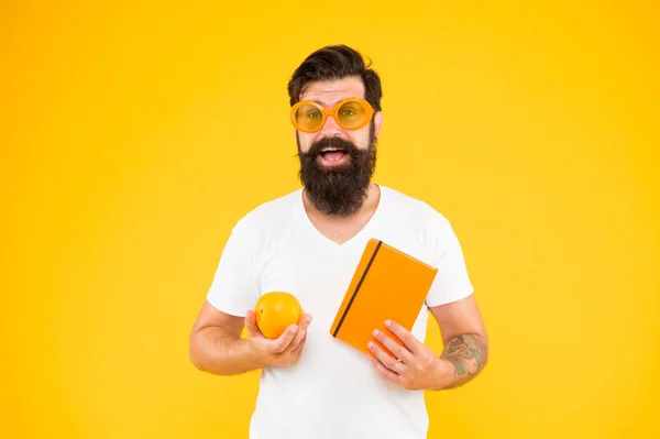 Essere orgogliosi di essere geek in te. Che secchione. Uomo barbuto in occhiali geek tenendo arancione e libro su sfondo giallo. Hipster in stile geek chic scegliere cibo sano per il cervello — Foto Stock