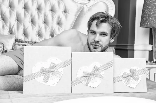 Des cadeaux pour tous. Bel homme avec des boîtes-cadeaux le matin de l'anniversaire. Homme sexy avec des cadeaux d'anniversaire couché dans le lit. L'homme barbu a des cadeaux emballés dans des boîtes. Présentation de cadeaux — Photo