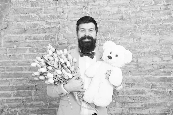 bearded man with gifts. Womens day. Spring gift. Bearded man hipster with flowers. Love date. international holiday. March 8. Bearded man with tulip bouquet and bear. spring happiness. man in love