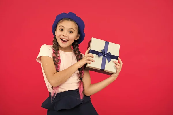 Los mejores regalos de Navidad. Una niña emocionada por desempacar su regalo. Niño niña sostiene caja de regalo con cinta sobre fondo rojo. Regalo de Navidad para hija. Pequeña linda chica recibió regalo de vacaciones —  Fotos de Stock