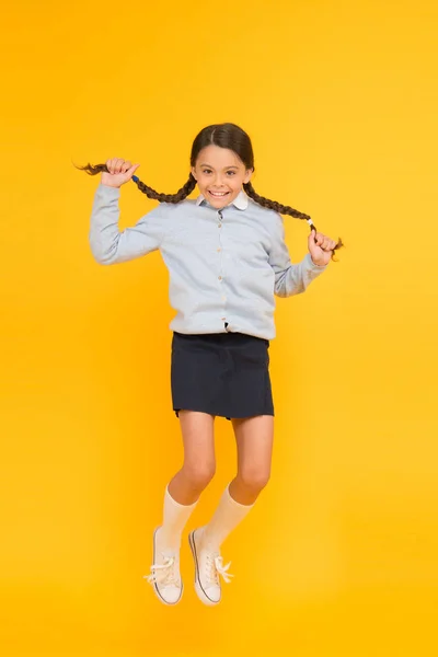 Elle est hyper. Joyeux gosse énergique sautant sur fond jaune. Petite fille aux cheveux longs tresses se sentant énergique. Petit écolier qui commence énergiquement l'année scolaire. Actif et énergique — Photo