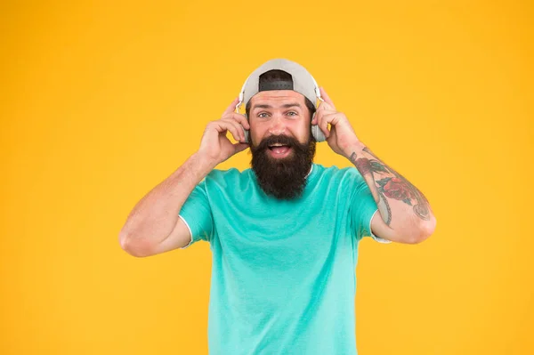 Hay música para cada hombre. Hombre barbudo en estilo hipster de moda sonriendo sobre fondo amarillo. Hombre feliz con barba y bigote usando auriculares modernos. Brutal hombre disfrutar escuchando música — Foto de Stock