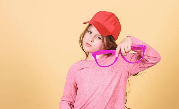 Um acessório elegante. Sentindo-se confiante com acessórios. Menina bonito criança usar boné ou chapéu snapback segurar óculos fundo bege. Menina vestindo boné de beisebol brilhante. Chapéu ou boné. Moda moderna — Fotografia de Stock