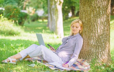 Dizüstü bilgisayar işleriyle açık havada ağaç gövdesinde yağsız olan kadın. Park içinde laptop ile kız iş çimenlerin üzerinde oturmak. Doğal çevre ofisi. Açık havada faydaları iş. Eğitim teknolojisi ve internet kavramı