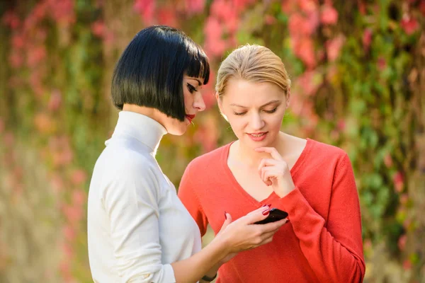 Las chicas se comunican mirando el teléfono. Concepto de redes sociales. Enlace compartido. Compra en línea. Tecnología moderna. Navegar por Internet. Comunicarse en línea. Dos mujeres con smartphone que se comunican al aire libre —  Fotos de Stock