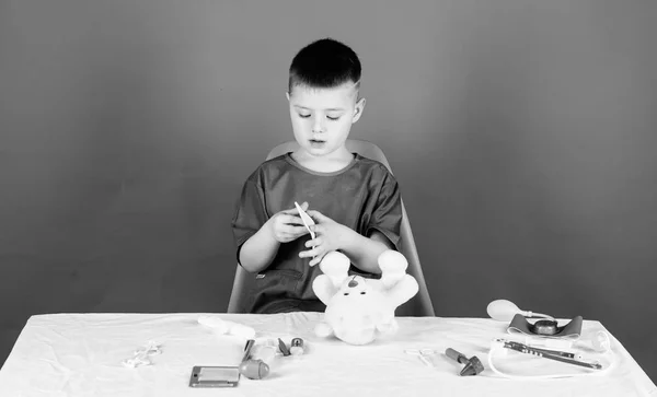 Hospital worker. Health care. Kid little doctor busy sit table with medical tools. Medical examination. Medicine concept. Medical procedures for teddy bear. Boy cute child future doctor career