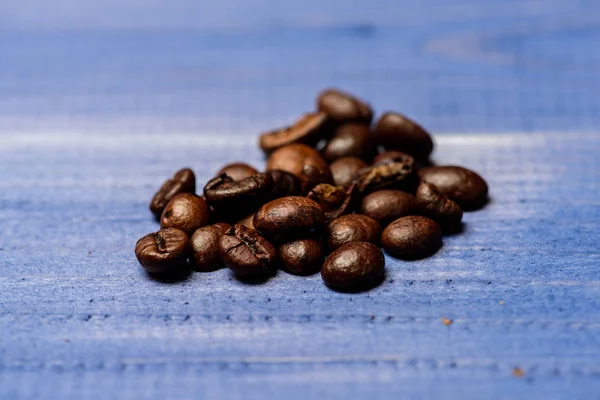 Coffee shop or store. Fresh roasted coffee close up. Pile beans on blue wooden background. Degree of roasting coffee beans. Coffee for inspiration and energy charge. Texture and background concept