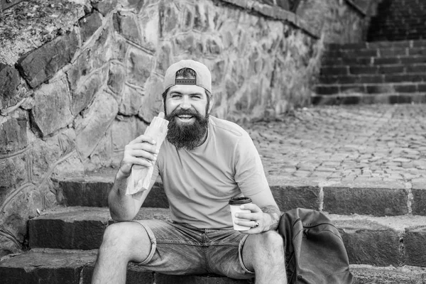 Hungry man snack. Junk food. Guy eating hot dog. Man bearded enjoy quick snack. Street food so good. Urban lifestyle and unhealthy nutrition. Carefree hipster eat junk food while sit on stairs