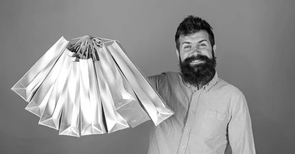 Man with beard and mustache holds shopping bags, red background. Hipster on happy face is shopping addicted or shopaholic. Guy shopping on sales season with discounts. Shopping concept — Stock Photo, Image