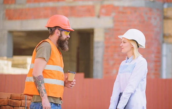 Relationships between construction clients and participants of building industry. Woman engineer and brutal builder communicate construction site background. Construction team communication concept