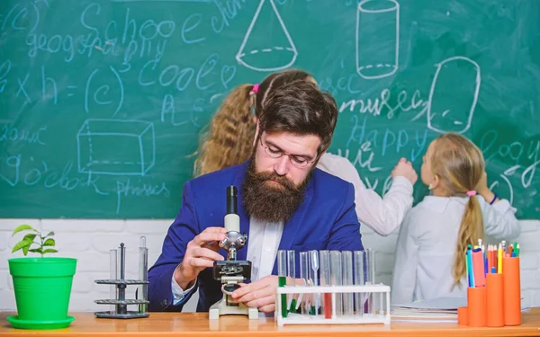 Explaining biology to children. Biology plays role in understanding of complex forms of life. School teacher of biology. Man bearded teacher work with microscope and test tubes in biology classroom