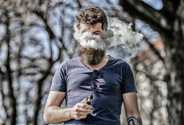 Sakallı adam vape içiyor. Elektronik sigara içiyor. Adam uzun sakal sigara alışkanlığı ile rahat. Sakallı ve bıyıklı adam duman solur. Beyaz aromalı duman bulutları. Stres giderme konsepti