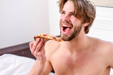 Yatakta pizza ile gömleksiz seksi adam Kırpılmış görüntü. Adam sakallı yakışıklı adam yatakta kahvaltı için peynirli yemek yiyor. Evde çıplak ve pizzayla dinlenen genç bir adam. Yatakta Pizza.