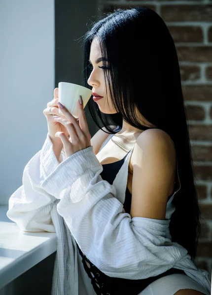 Passionate mysterious lover. Perfect coffee time. But first coffee. Enjoying morning sunlight. Sensual girl sexy breasts drinking coffee near windowsill. Attractive female lingerie relaxing at home — Stock Photo, Image