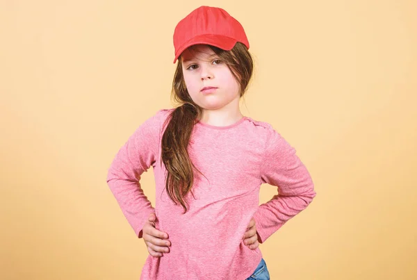 Cutie in cap. Kids fashion. Feeling confident with this cap. Girl cute child wear cap or snapback hat beige background. Little girl wearing bright baseball cap. Modern fashion. Stylish accessory