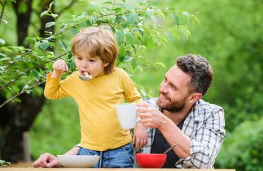 Baba oğul yemek yer ve eğlenir. Çocuklar için menü. Aile ev yapımı yemeklerin tadını çıkarır. Yemek alışkanlıkları. Baba ile küçük çocuk yemek piknik bahçesinde doğa arka plan yiyor. Yaz kahvaltısı. Sağlıklı gıda kavramı