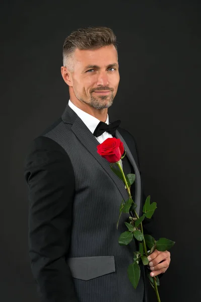 Feliz dia das mulheres. Homem elegante segurando rosa vermelha no dia das mulheres. Homem bonito em terno formal e gravata preta celebrando o dia das mulheres. 8 de março ou celebração internacional do dia das mulheres — Fotografia de Stock