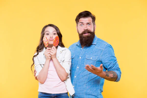 Sharing sweets with dearest people. Girl child and dad hold colorful lollipops. Sweet dessert. Bearded hipster good daddy for adorable daughter. Daughter and father eat sweet candies. Sweet childhood