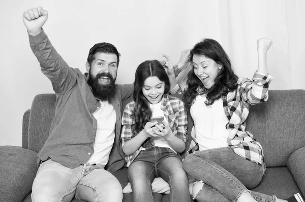 Family spend weekend together. Child little girl use smartphone with parents. Friendly family having fun together. Mom dad and busy daughter relaxing on couch. Family leisure. Parental advisory