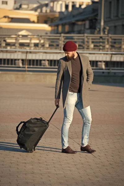 Anpassung des Lebens in der neuen Stadt. Reisende mit Koffer kommen Flughafen Bahnhof urbanen Hintergrund. Hipster sind reiselustig. Tragetasche. Mann bärtiger Hipster reist mit Gepäcktasche auf Rädern — Stockfoto