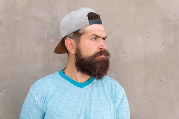 Hairy and bearded. Brutal hipster with thick mustache and beard hair on unshaven face. Hipster on grey wall. Bearded man in trendy hipster style. Caucasian hipster wearing casual baseball cap — Stock Photo, Image