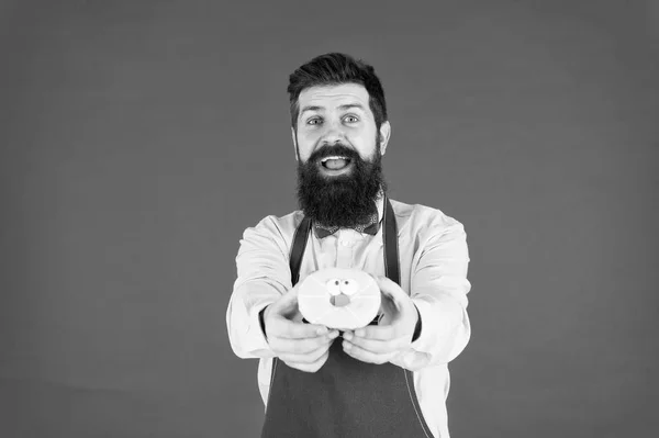 Mit Liebe gebacken. Hipster bärtige Bäcker halten glasierten Donut auf rotem Hintergrund. Café und Bäckereikonzept. süßer Donut vom Bäcker. Mann bärtigen Bäcker in Schürze halten niedlichen Nachtisch. Privatbäckerei — Stockfoto