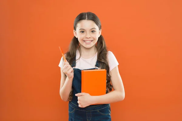 Forskning. litteratur lektion. tillbaka till skolan. lycklig liten flicka med anteckningsboken. Skolflicka Läs bok på Orange bakgrund. skriva anteckningar. Kid dagbok. poesi och roman. modern utbildning — Stockfoto