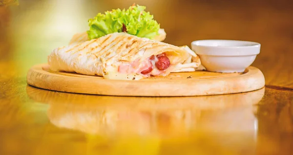 Restaurant food concept. Lavash burrito stuffed meat sausage and cheese sauce served salad. Meat wrapped with lavash burrito. Restaurant meal traditional cuisine. Burrito tortilla served wooden board