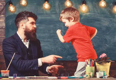 Öğretmen sakal, baba ve küçük oğul having oyunculuk sınıfında, kara tahta arka plan ile. Babalık kavramı. Neşeli çocuk ve resim, çizim öğretmen. Yetenekli sanatçı oğlumla vakit geçirmek