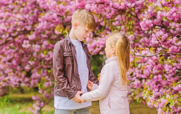 Una cita romántica en el parque. Primavera para enamorarse. Los niños enamorados flor de cerezo rosa. El amor está en el aire. Un par de adorables niños encantadores caminan por el jardín de sakura. Tiernos sentimientos de amor. Niña y niño —  Fotos de Stock