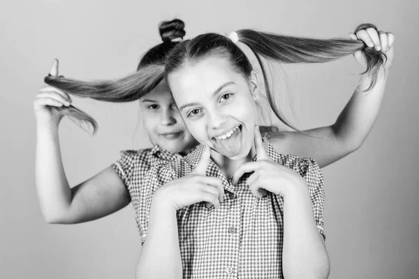 Естественные наращивания волос. Маленькая девочка держит длинные волосы своей сестры. Маленькая девочка улыбается с светлыми волосами. Симпатичный счастливый ребенок с модными хвостиками — стоковое фото